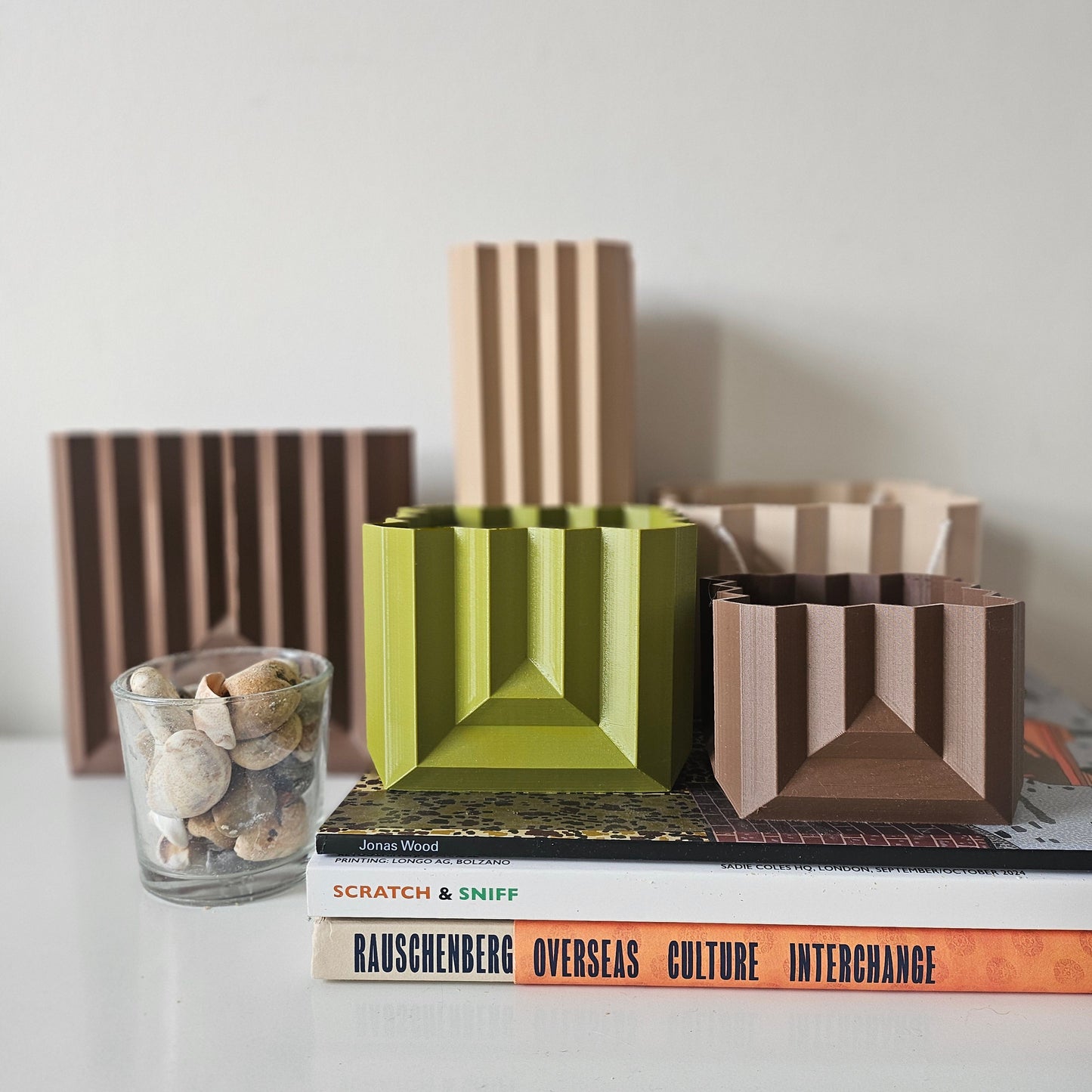 Geometric vases and planters on a shelf with books and a glass container.