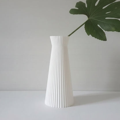 A white ribbed vase with a flared top, holding a single green monstera leaf, set against a minimalist light gray background.
