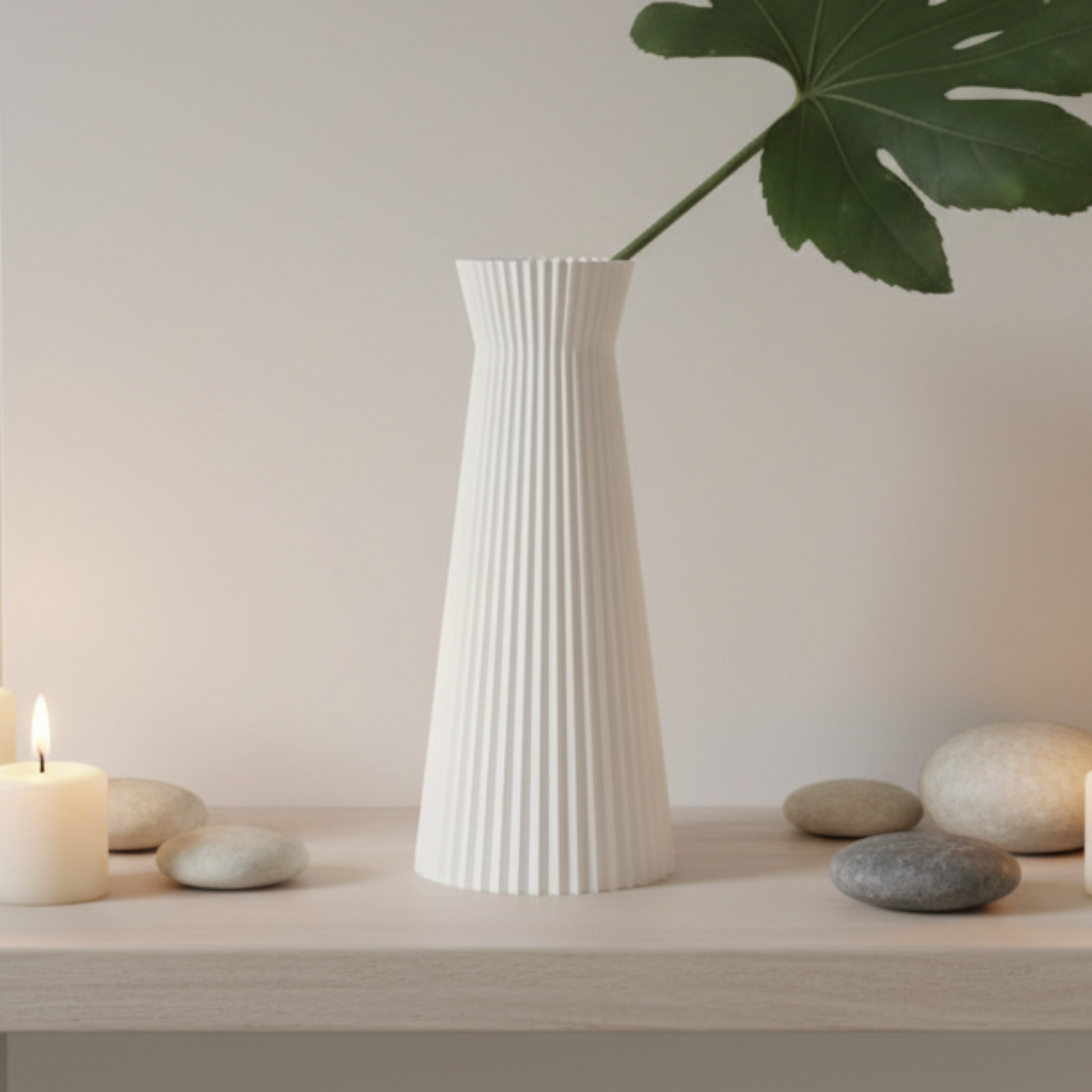 A white ribbed vase with a flared top, holding a green monstera leaf, displayed on a light wooden shelf with candles and smooth stones against a warm beige wall.