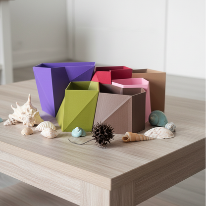 A set of colorful geometric planters in purple, green, brown, pink, beige and red, styled on a light wood table with seashells and a sea urchin.