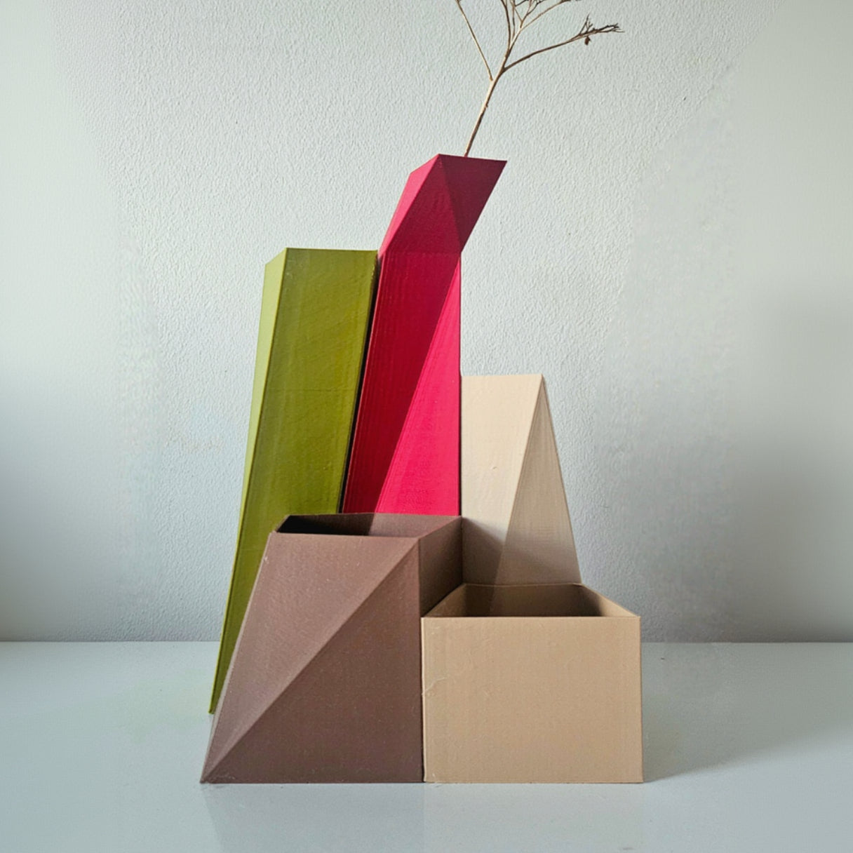 Three geometrically shaped vases in red, green, and brown on a white surface with a light gray background.